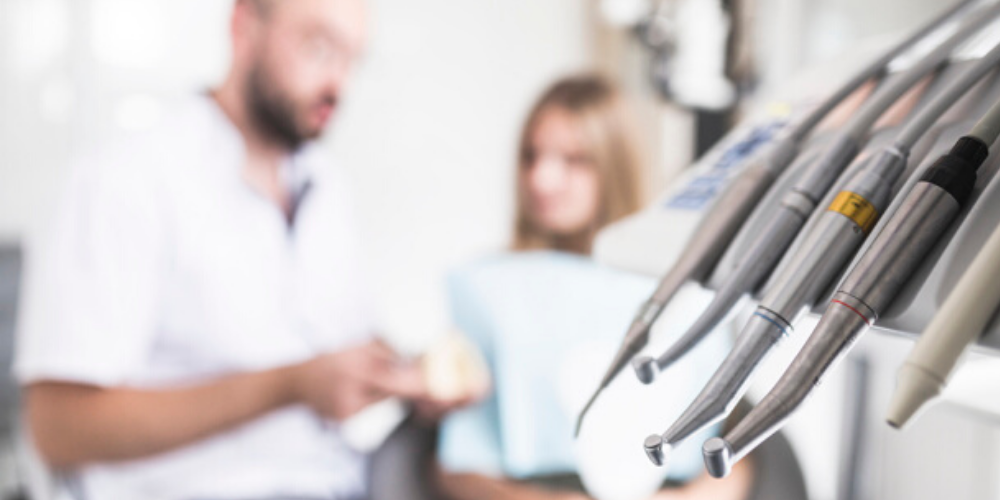 Herramientas de un dentista y al fondo un dentista hablando con una paciente