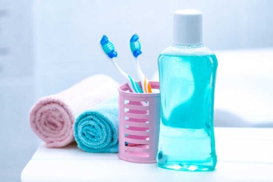 Una botella de enjuague bucal, unas toallas y un bote con cepillos de dientes