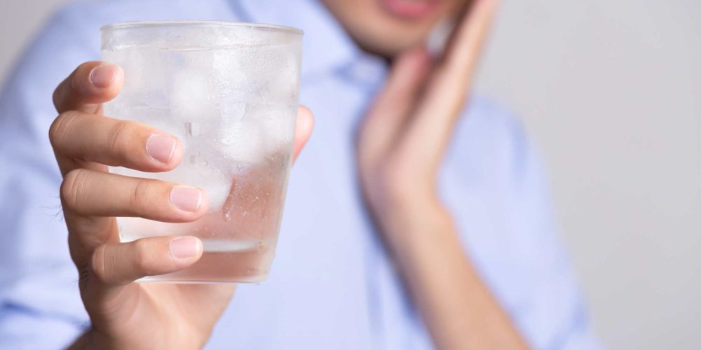 Joven con dientes sensibles. En la mano sostiene un vaso agua fría hielo